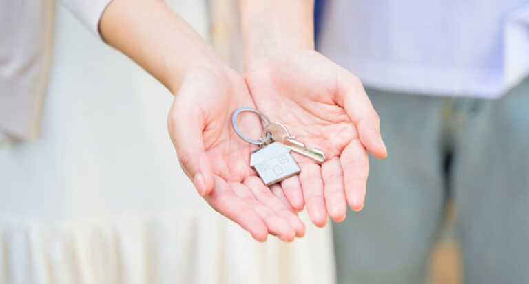 Key with a house-shaped keychain held in an open hand, symbolizing new home ownership or real estate transaction.
