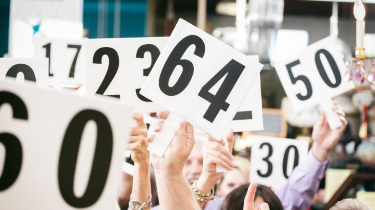 People with raised hands in the air with numbers on signs for bidding at an auction house